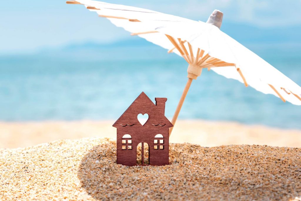 figura de una casa con una sombrilla sobre la arena de la playa