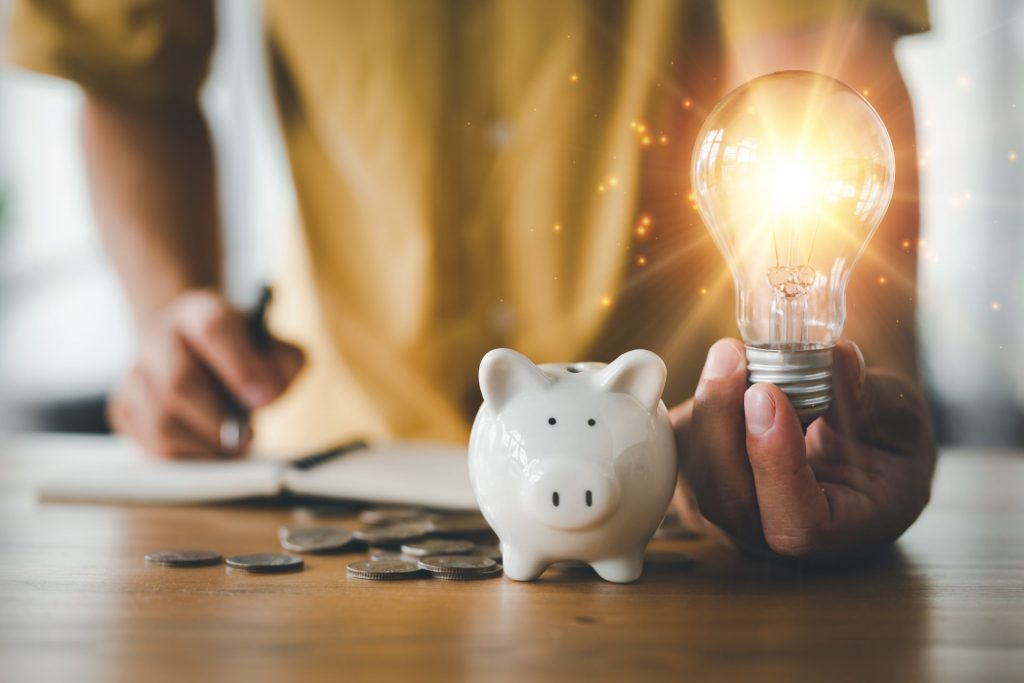 Persona sujetando una bombilla y una hucha representando el ahorro de energía en casa