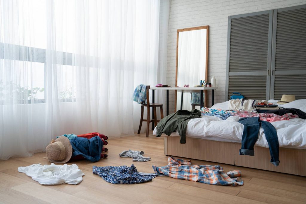 Habitación desordenada con ropa sobre el suelo y sobre la cama