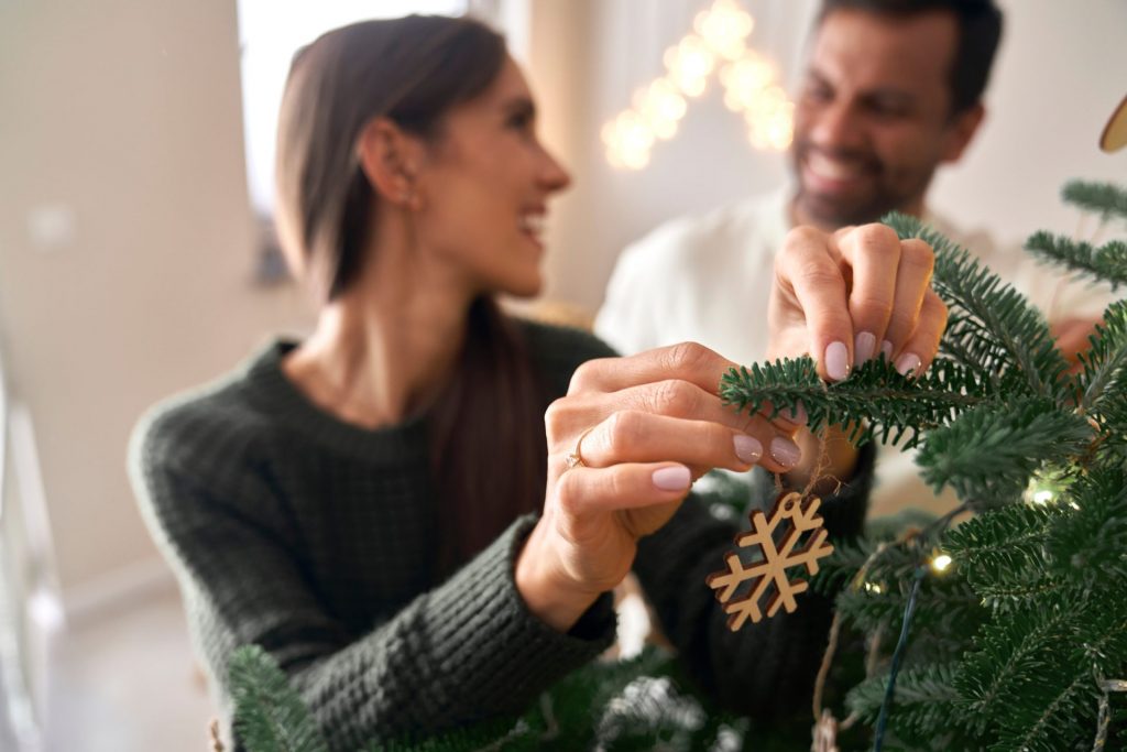 Pareja sonriendo y poniendo adornos de decoración navideña casera en un árbol de navidad
