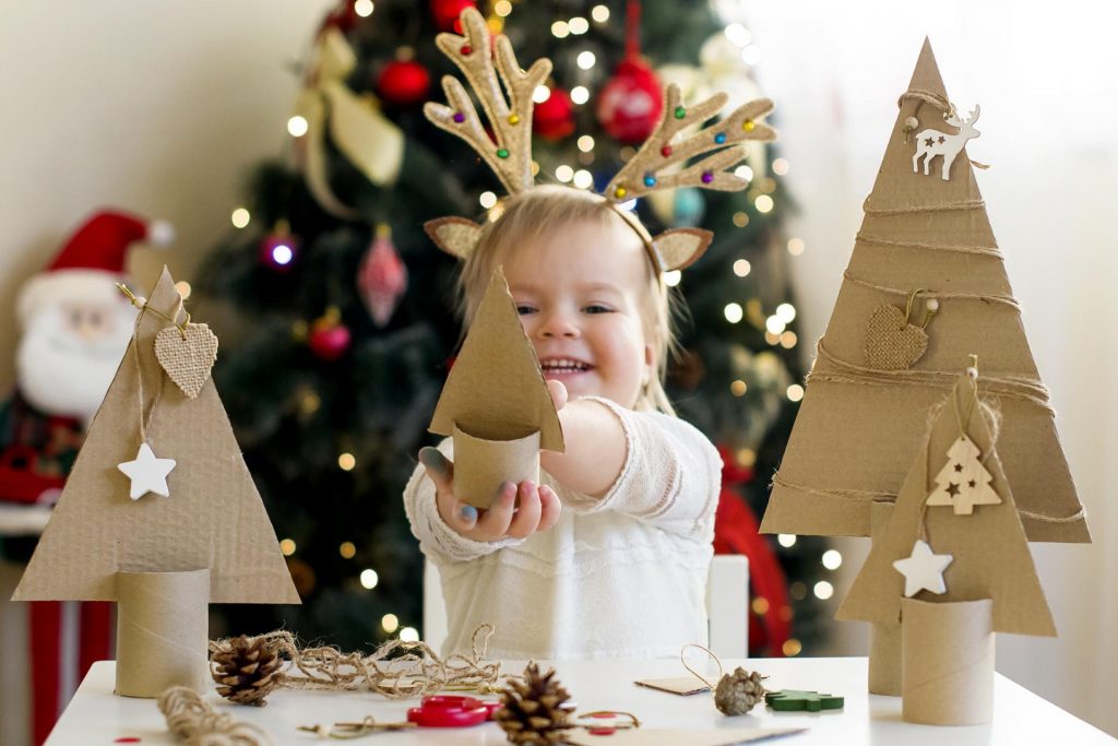 Niña pequeña sonriendo haciendo elementos de decoración navideña casera