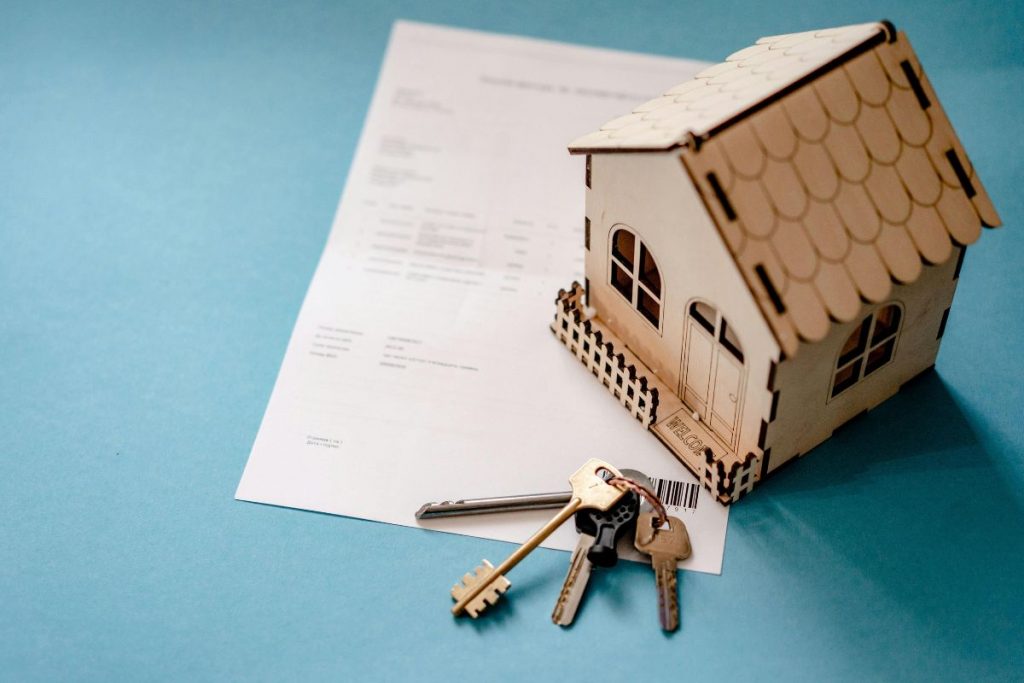 documento de una hipoteca y encima unas llaves de una vivienda junto con una pequeña casa de madera de decoracion 