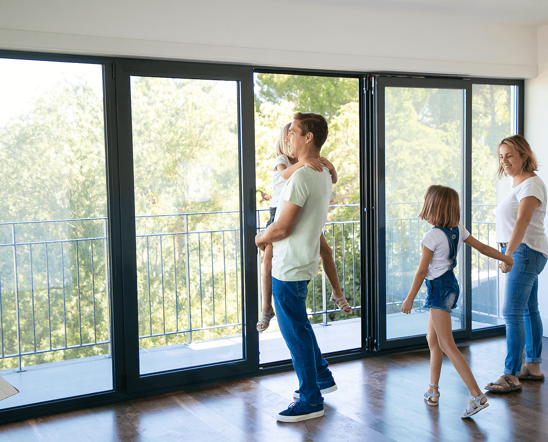 padre feliz con hija de pie cerca de balcon abierto y sonriendo