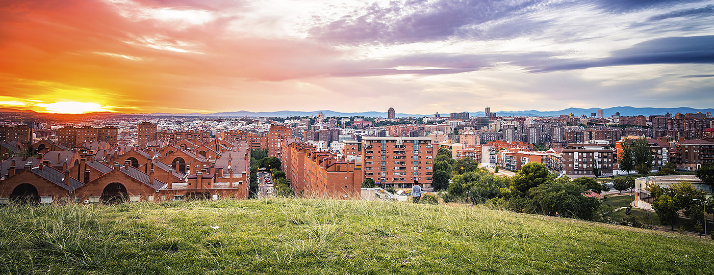 Guía para vivir en Vallecas: zonas recomendadas, transporte y calidad de vida 3 Vista panorámica del barrio de Vallecas desde el Cerro del Tío Pío al atardecer, con bloques de viviendas de ladrillo bajo un cielo de tonos anaranjados y las montañas de la sierra al fondo